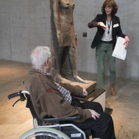 Mann im Rollstuhl vor einer ägyptischen Statue