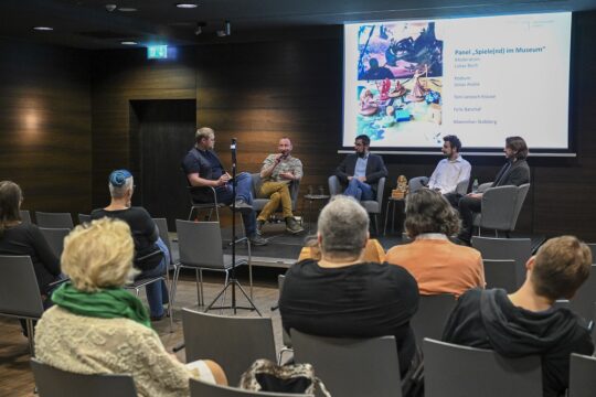 Auf einem Podium sitzen vie menschen, vor ihnen eine Gruppe von Menschen im Publikum.