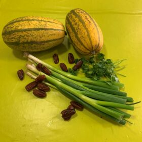 auf einem hellgrünen Tisch liegen zwei Kürbisse, ein Bündel Lauch und einige Rosinen