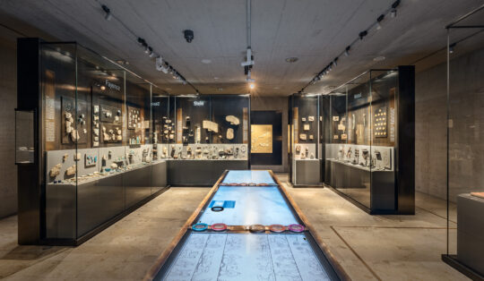 Blick in den Raum Kunsthandwerk. Außen ein Viereck von Vitrinen, in der Mitte eine große, tischartige Medienstation