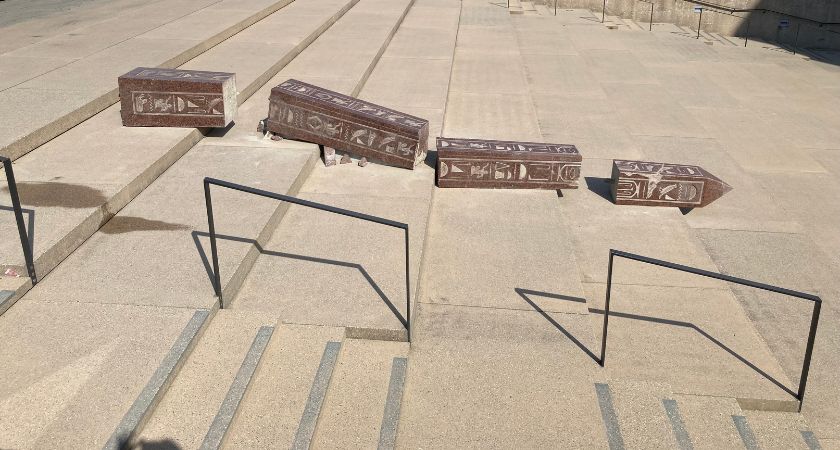 Auf der großen Außentreppe des Museums liegen über mehrere Stufen verteilt einzelne Bruchstücke eines Obelisken aus rötlichem Stein. Es macht den Anschein, als sei der Obelisk die Treppe hinabgestürzt.