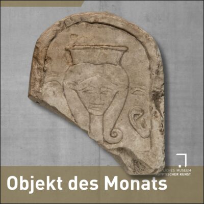 Halbrunde Stele aus hellem Stein, linke untere Seite abgebrochen. Auf der Stele in erhabenem Relief das gesicht einer Frau mit Zöpfen, die unten in Schneckenform auslaufen. In der rechten unteren Ecke der Stele ein Ohr.