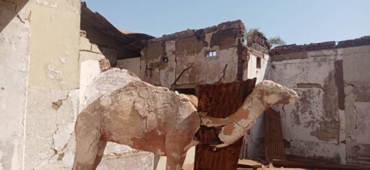 Zerstörte Statue eines Kamels vor einem zerstörten gebäude