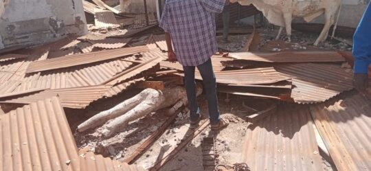 Ein Mensch steht in einem zerstlrten Raum, rund um ihn Wellblech von einem Dach