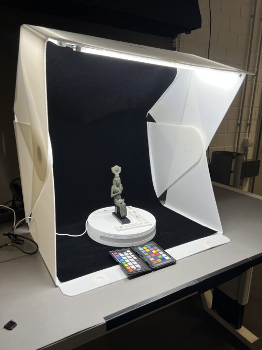 In einer Fotobox steht eine kleine altägyptische Statue.